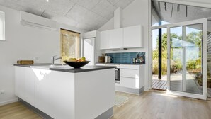 Une cuisine moderne dotée d’un îlot central, de meubles blancs et offrant une vue sur un jardin grâce à une porte-fenêtre coulissante.