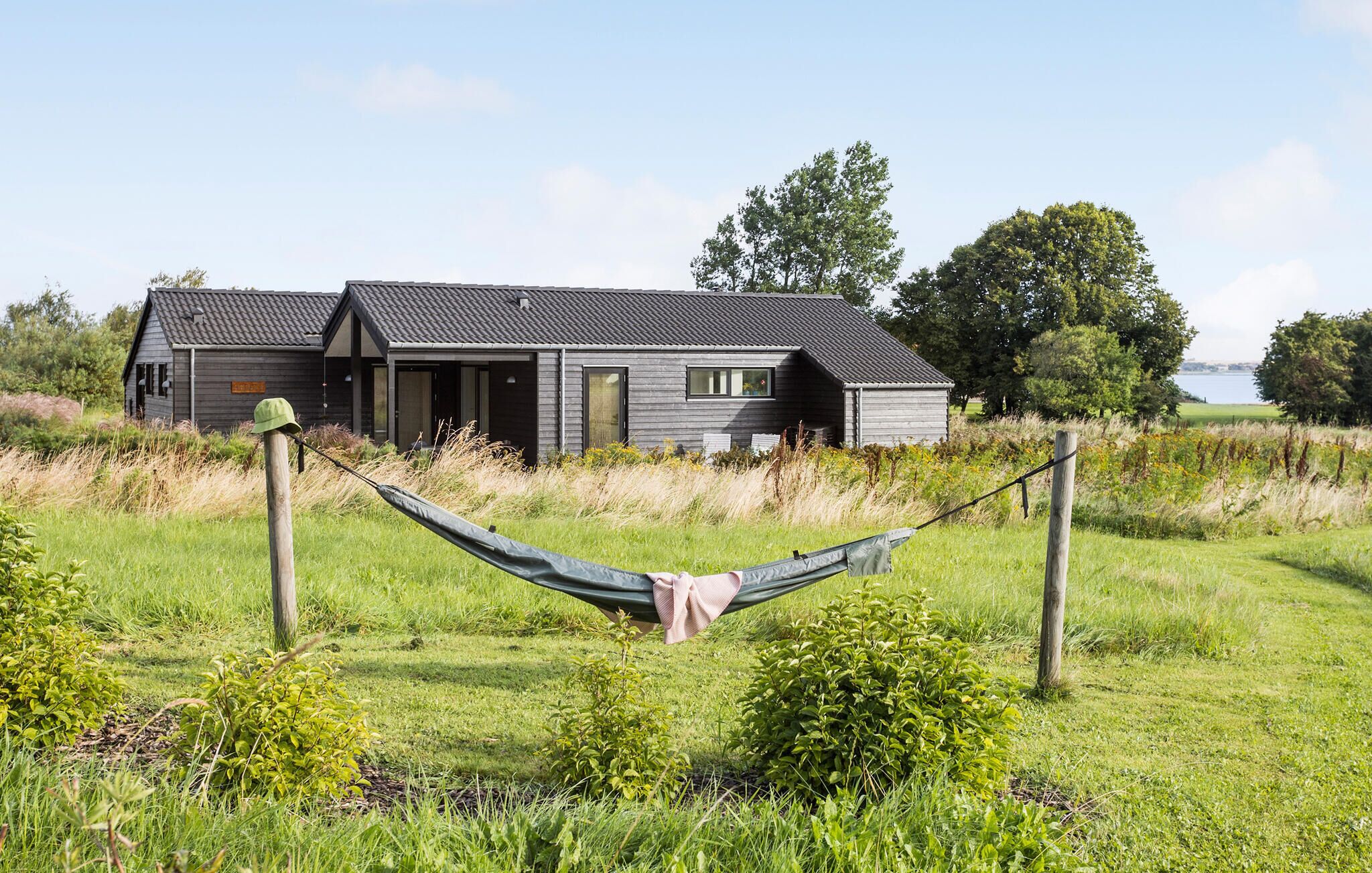 Ein modernes Haus mit grauem Dach und dunklen Verkleidungen, umgeben von einer grünen Wiese und Bäumen.