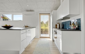 Une cuisine moderne avec des meubles blancs, une grande fenêtre et une vue sur la verdure.