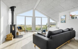 Uma sala de estar moderna com um amplo sofá cinzento, uma mesa de centro de madeira e uma lareira preta.