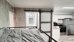 A bedroom with a bed, wooden walls, a sliding door, and a kitchen area with appliances. - Cozy spot near Lake Winnie, studio in Rossville, WiFi, AC and privacy (Rossville)