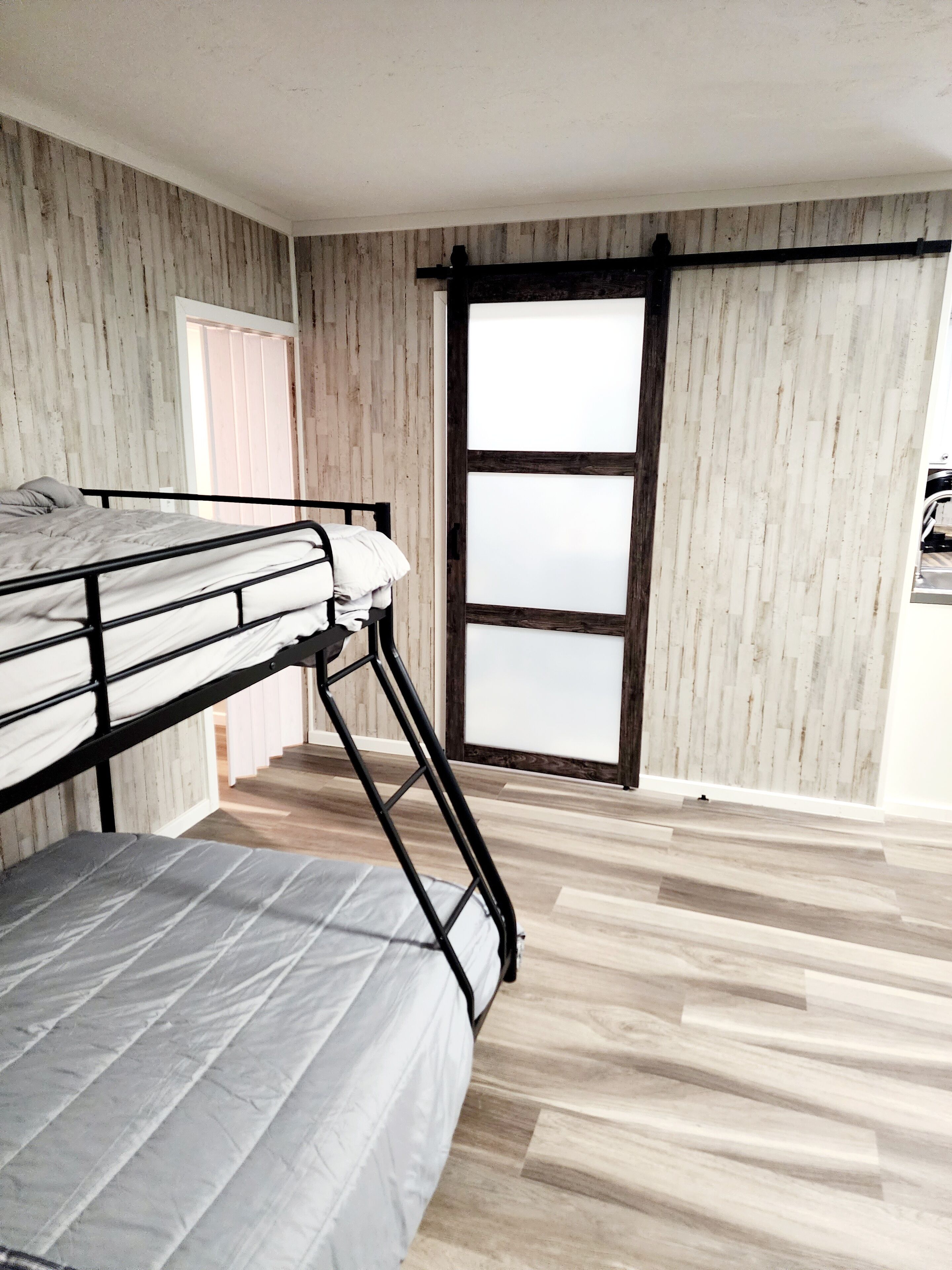 Una habitación con una litera, paredes de paneles de madera, una puerta corrediza de vidrio y piso de madera.
