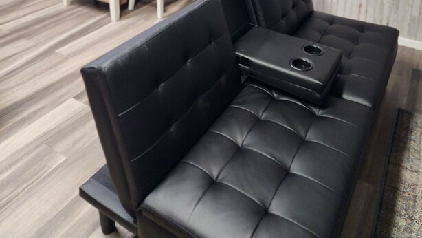 A modern living room with a black leather sofa, a small wooden table, and a chair. A door with a decorative panel is visible in the background. - Cozy spot near Lake Winnie, studio in Rossville, WiFi, AC and privacy (Rossville)