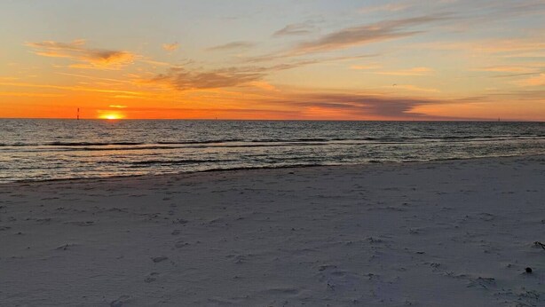 Ranta, josta avautuu näkymä auringonlaskuun meren yllä.
