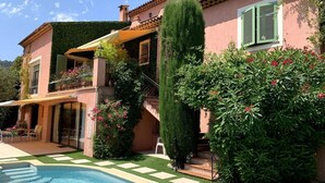 Una casa a due piani con piscina, persiane verdi e patio coperto.
