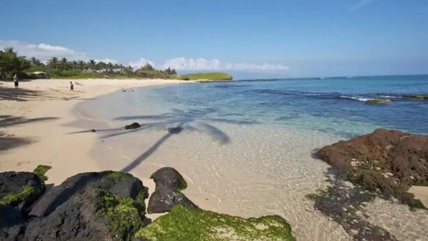 A beach with clear water, rocks, and a few people.