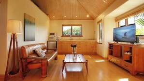 A spacious living room with a wooden ceiling, a leather sofa, a coffee table, and a television on a wooden stand.