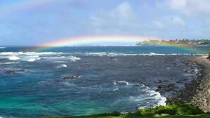 A coastal view with a rainbow over the ocean and a rocky shoreline.