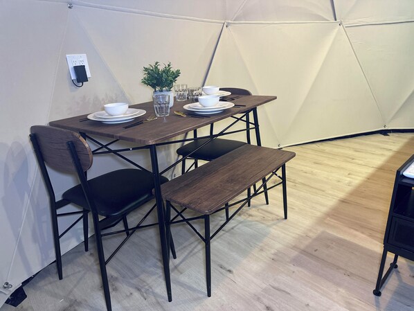 A dining area with a table set for four, including plates, bowls, glasses, and cutlery. There is a bench at the table, and the room has a tent-like structure with a light-colored floor.