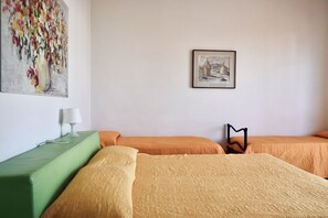 Une chambre d’hôtel avec deux lits, un canapé vert, une lampe et deux tableaux au mur.
