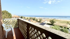Un balcón con vista a la playa, paneles solares y una silla de plástico blanca.