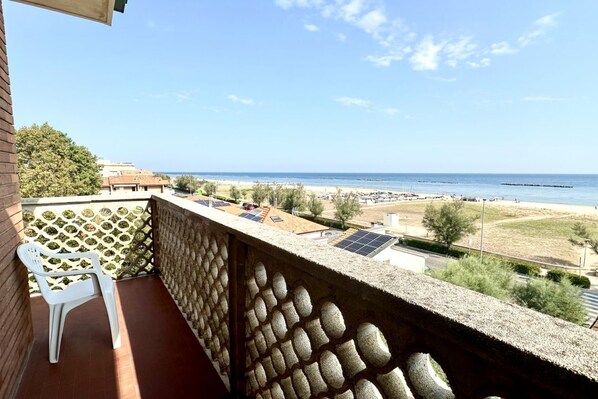 A balcony with a view of the beach, solar panels, and a white plastic chair.