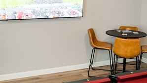 Biljardipöytä, biljardipalloja, biljardikeppi ja televisio, josta näkyy urheilutapahtuma. Pienen pöydän ympärillä on neljä tuolia.
