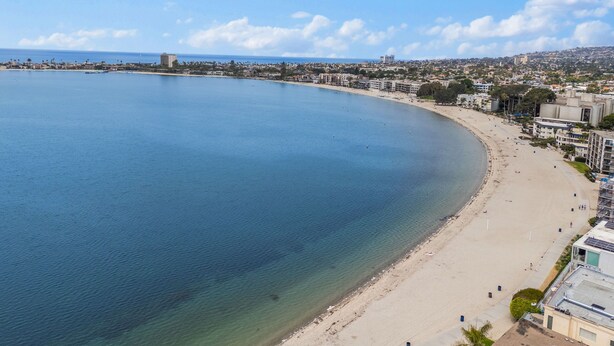 Paisagem costeira com uma praia extensa, água azul cristalina e uma mistura de edifícios residenciais e comerciais.