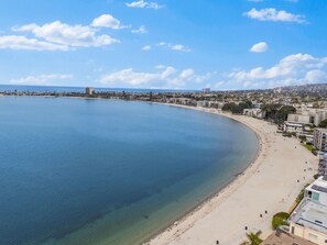 A coastal cityscape with a wide beach, clear blue water, and a mix of residential and commercial buildings.