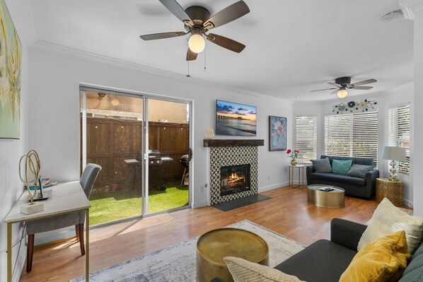 A living room with a fireplace, a ceiling fan, a sofa, and a dining area with a sliding glass door leading to a backyard.
