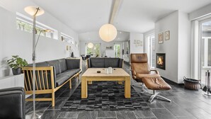 A modern living room with a sofa, a dining table, a leather armchair, and a fireplace. - 4 bedroom cozy home in ålbæk (Ålbæk)