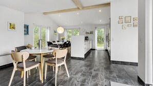 A modern kitchen with a dining area, featuring a large island, dark tiled flooring, and a view through the glass door. - 4 bedroom cozy home in ålbæk (Ålbæk)