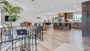A spacious living area with a staircase, a dining area, and a kitchen with dark wooden cabinets and a large island. - Colorado's Best (Colorado Springs)