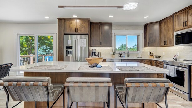 A modern kitchen with wooden cabinets, stainless steel appliances, and a central island with bar stools. - Colorado's Best (Colorado Springs)