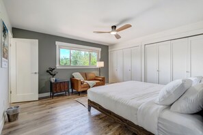 A bedroom with a wooden bed, a ceiling fan, a window with a view, a small table with a plant, and a chair. - Colorado's Best (Colorado Springs)