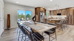 A modern kitchen with wooden cabinets, a central island, and a dining area with a long table and chairs. - Colorado's Best (Colorado Springs)