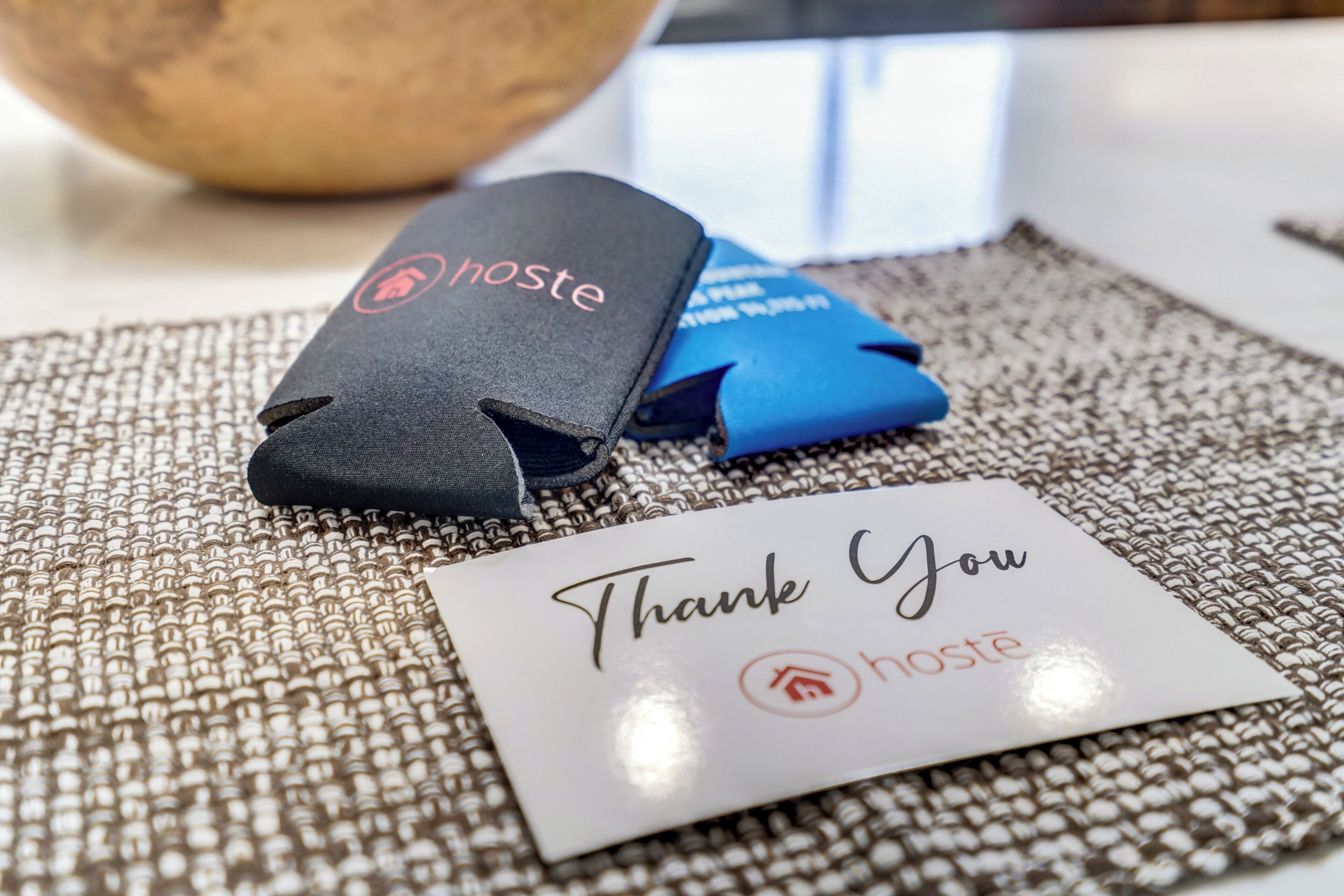 A thank you card and two small black objects with the word "hoste" on them, placed on a textured surface.