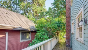 A wooden deck with a white railing, adjacent to a red building with a green roof and a brick chimney.