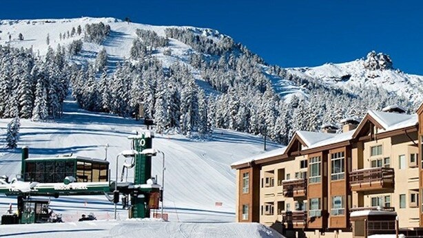 A snow-covered mountain with a ski lift and a row of wooden buildings with balconies. - Mountain Club | Premium 1BR Condo | Fireplace (Kirkwood)