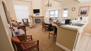 A cozy living room with a fireplace, a dining area, and a kitchen with a bar. - Mountain Club | Premium 1BR Condo | Fireplace (Kirkwood)