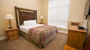 A bedroom with a large bed, two bedside tables, a nightstand, a wooden dresser, and a window with blinds. - Mountain Club | Premium 1BR Condo | Fireplace (Kirkwood)