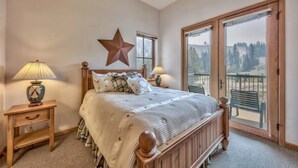 Une chambre avec un lit en bois, deux tables de chevet avec des lampes, une décoration en forme d’étoile sur le mur et une grande fenêtre donnant sur les arbres.