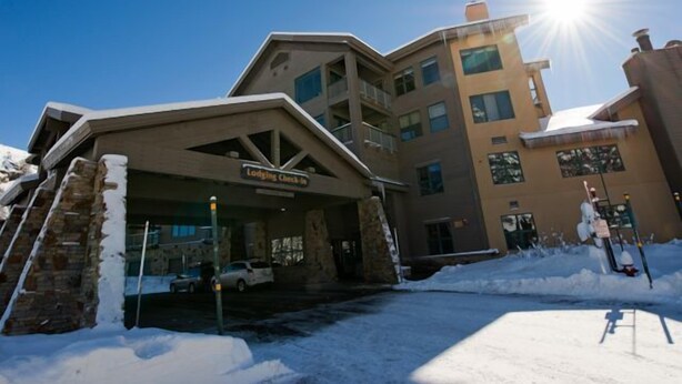 L’entrée d’un hôtel, avec une pancarte indiquant « Enregistrement des clients », une façade en pierre et un sol recouvert de neige.