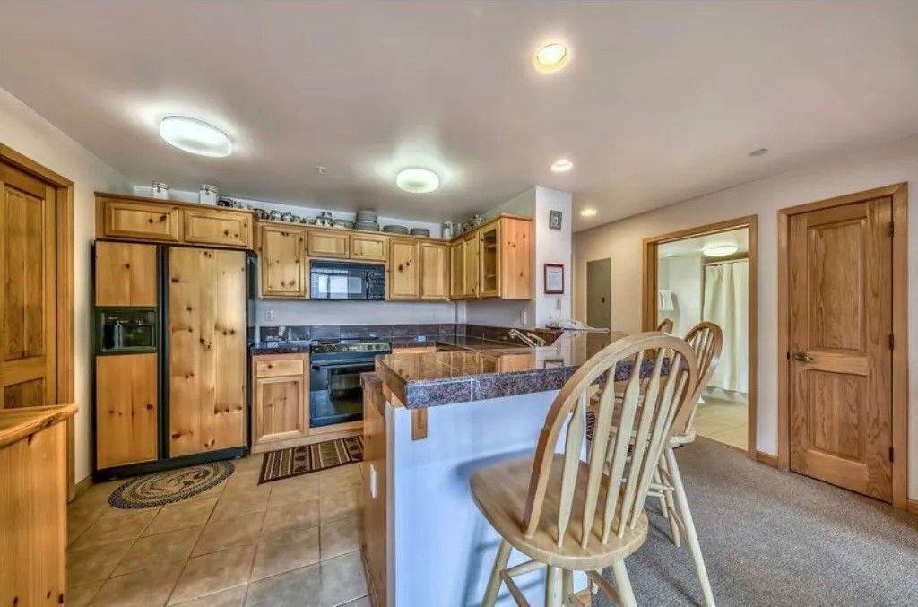 Une cuisine avec des meubles de rangement en bois, un four encastré et un coin bar avec un tabouret.
