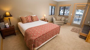 A bedroom with a large bed, two bedside tables, a chair, and a window.