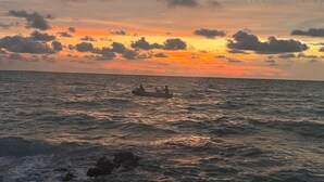 Een zonsondergang boven de oceaan met een boot en mensen in het water.