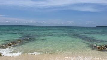 Ein Strand mit klarem türkisblauem Wasser, einem sandigen Ufer und einer entfernten Landmasse.