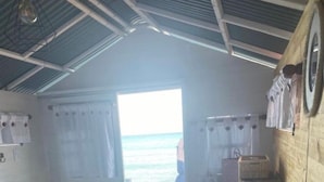 Een kamer met een bed, houten wanden, uitzicht op zee en een deur naar buiten.
