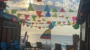 Een zitgedeelte aan het strand, met kleurrijke driehoekige vlaggen, stoelen en een vlag met het ontwerp van de Colombiaanse vlag.