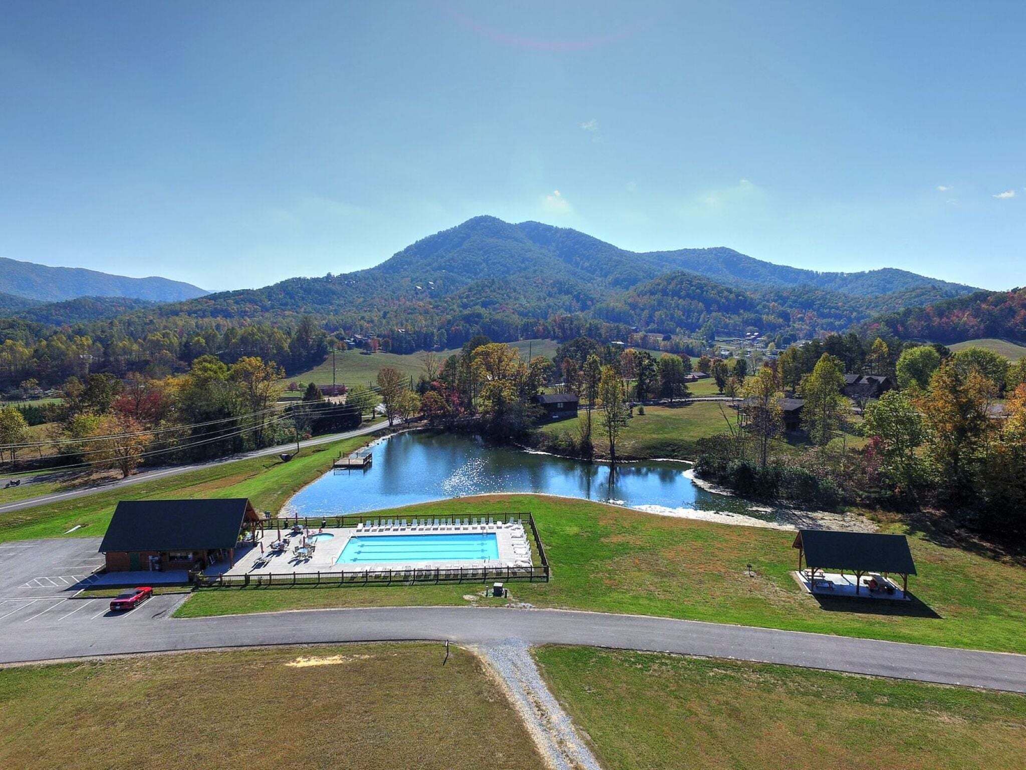 A swimming pool with a dock, surrounded by a grassy area and a mountain in the background.