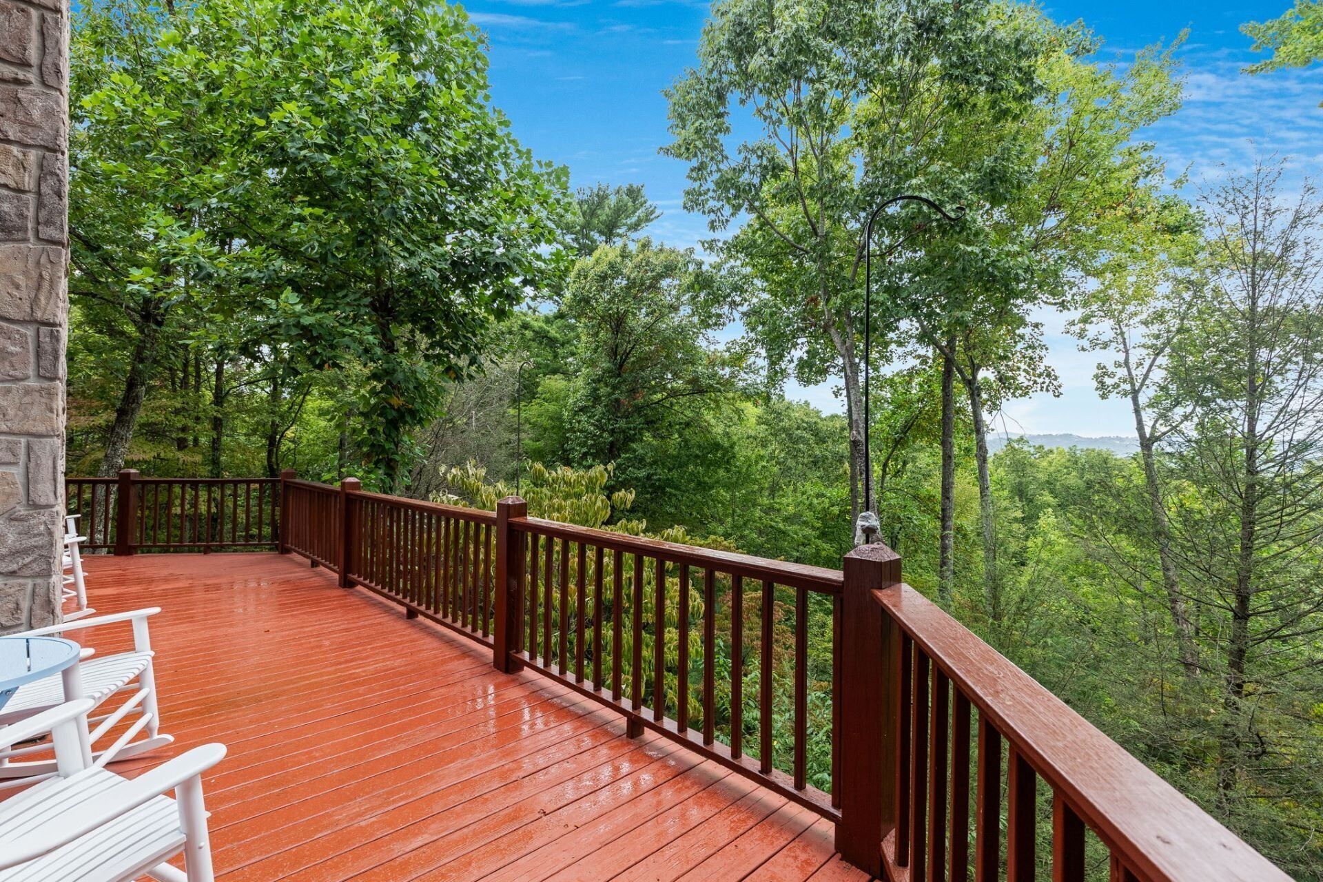 Une terrasse en bois avec une rambarde, entourée d’arbres et d’un mur de pierre.