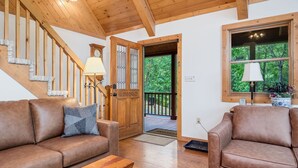Un salon chaleureux avec un escalier en bois, des canapés en cuir et une grande fenêtre donnant sur un paysage verdoyant.