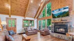 Un salon spacieux doté de planchers en bois, d’une cheminée et de grandes fenêtres offrant une vue sur l’extérieur.