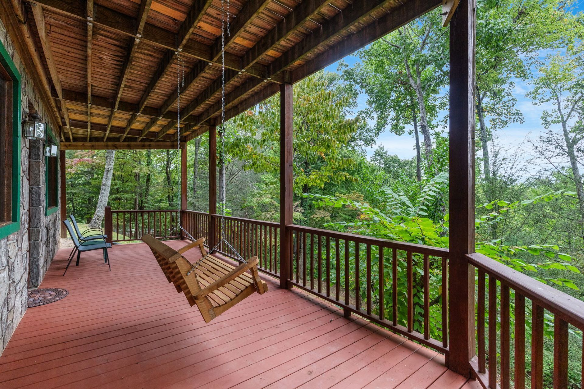 Un patio in legno con una poltrona a dondolo, pareti in pietra e vista su una zona boschiva.