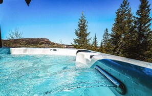 Un jacuzzi con agua cristalina azul, rodeado de árboles y una montaña al fondo.