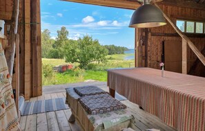 Une cabane en bois dotée d’une grande fenêtre donnant sur une zone herbeuse et un plan d’eau. On y trouve un lit avec une couvre-lit à motifs et une table agrémentée d’un arrangement floral.