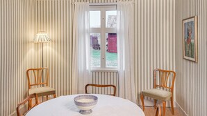 A room with striped wallpaper, a table with a bowl, two chairs, a lamp, and a window with a view of a red barn. - Awesome home in Frändefors (Frändefors)