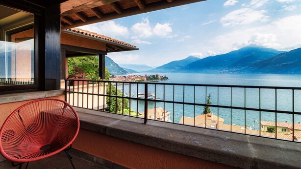 A balcony with a view of a lake and mountains, a red chair, and a railing. - Menaggio at its best - MyHomeinComo (Menaggio)