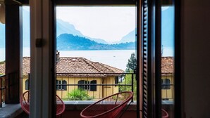 A balcony with a view of a lake and mountains, a yellow building with a tiled roof, and red chairs. - Menaggio at its best - MyHomeinComo (Menaggio)