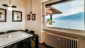 A dining area with a table, chairs, framed pictures on the wall, a window with a view of a lake and mountains, and a radiator. - Menaggio at its best - MyHomeinComo (Menaggio)